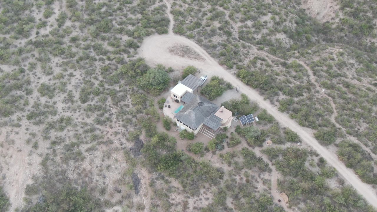 Overhead desert residence with solar panels and a curved dirt road.