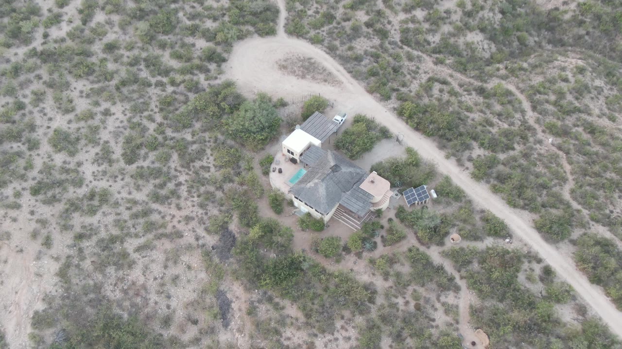 Aerial frame in Cabo Pulmo, Baja California Sur with the house compound near the lower left, solar panels to one side, dirt road above it, and no visible people.