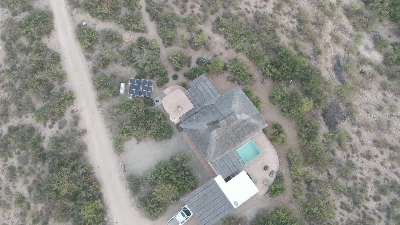 Overhead frame of a desert property, dirt road, solar panels, and white vehicle.