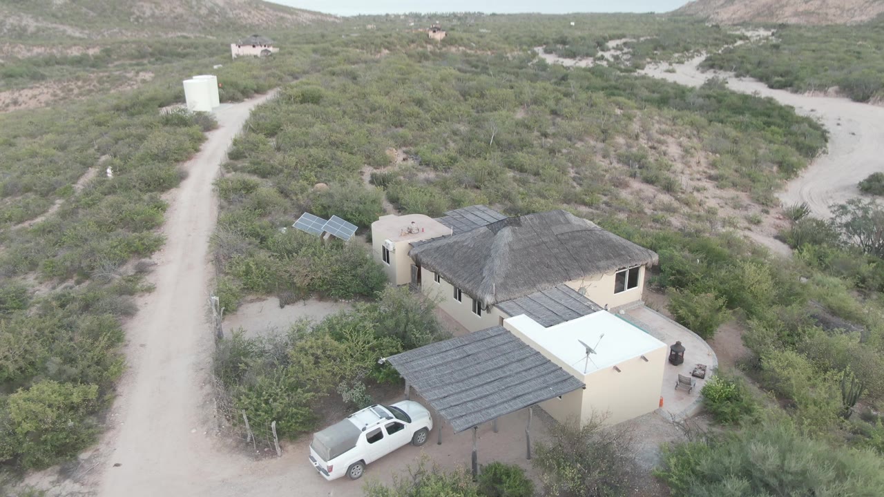 Aerial view of a house and truck below a dirt road with hills beginning to appear.