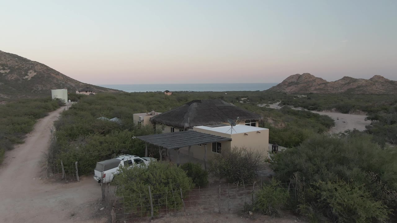 Coastal desert dirt road curves past a house with a white pickup nearby.