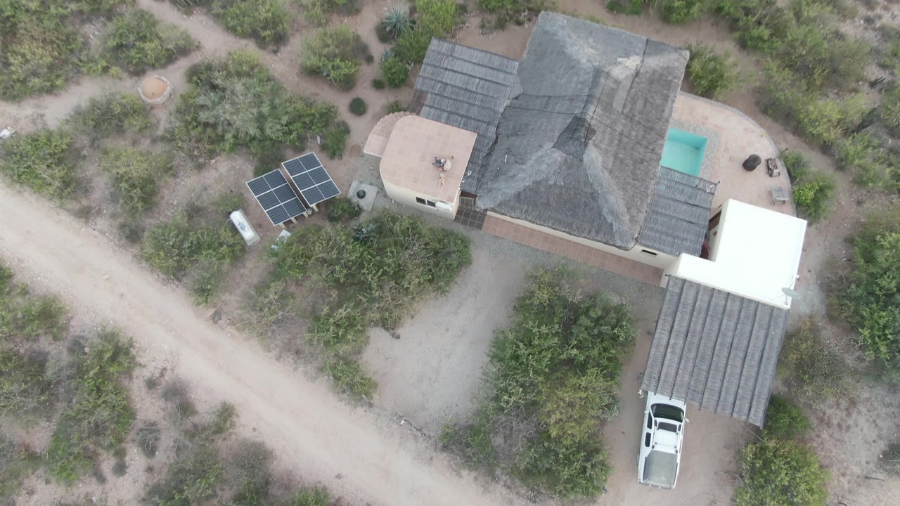 White vehicle begins to leave the covered carport beside the desert home.