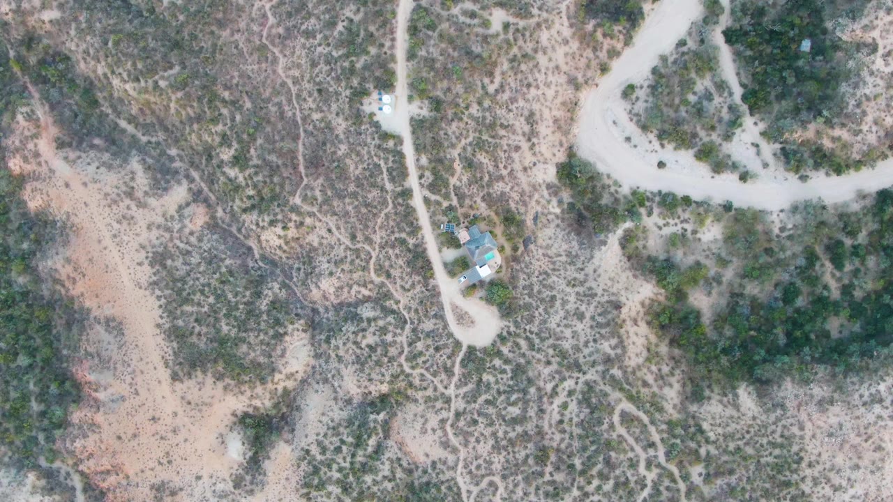 Overhead view of arid hillside with winding dirt road and small structure