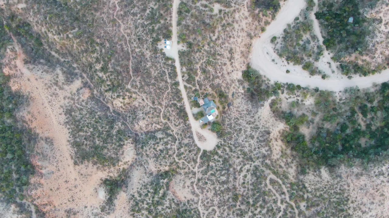 Opening overhead view in Cabo Pulmo, Baja California Sur, with pale dirt roads crossing scrubby desert and a small structure near the lower-left area, no visible people.