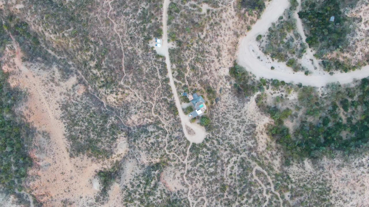 Overhead frame from Cabo Pulmo, Baja California Sur showing a pale dirt road, scrub-covered rocky ground, small structures near the lower road, and no visible people.