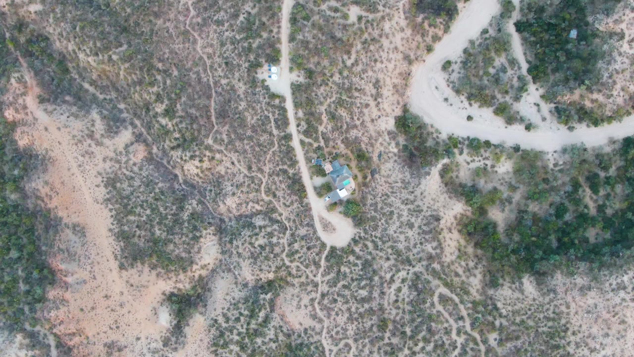 One second into the Cabo Pulmo aerial, the pale dirt road curves across scrub-covered hills beside a small isolated structure, with no visible people.