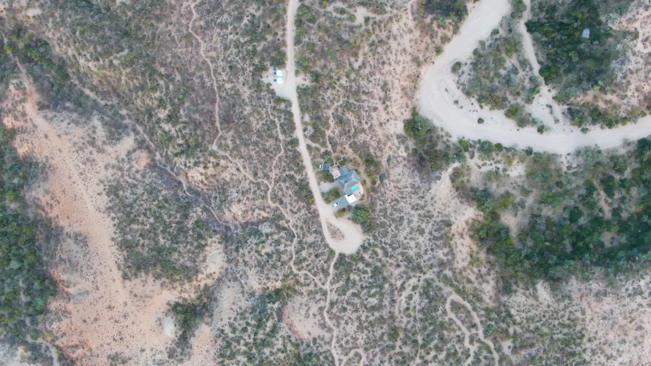 Overhead view in Cabo Pulmo, Baja California Sur showing rocky desert scrub, a pale dirt road, and a small building cluster near the road with no visible people.