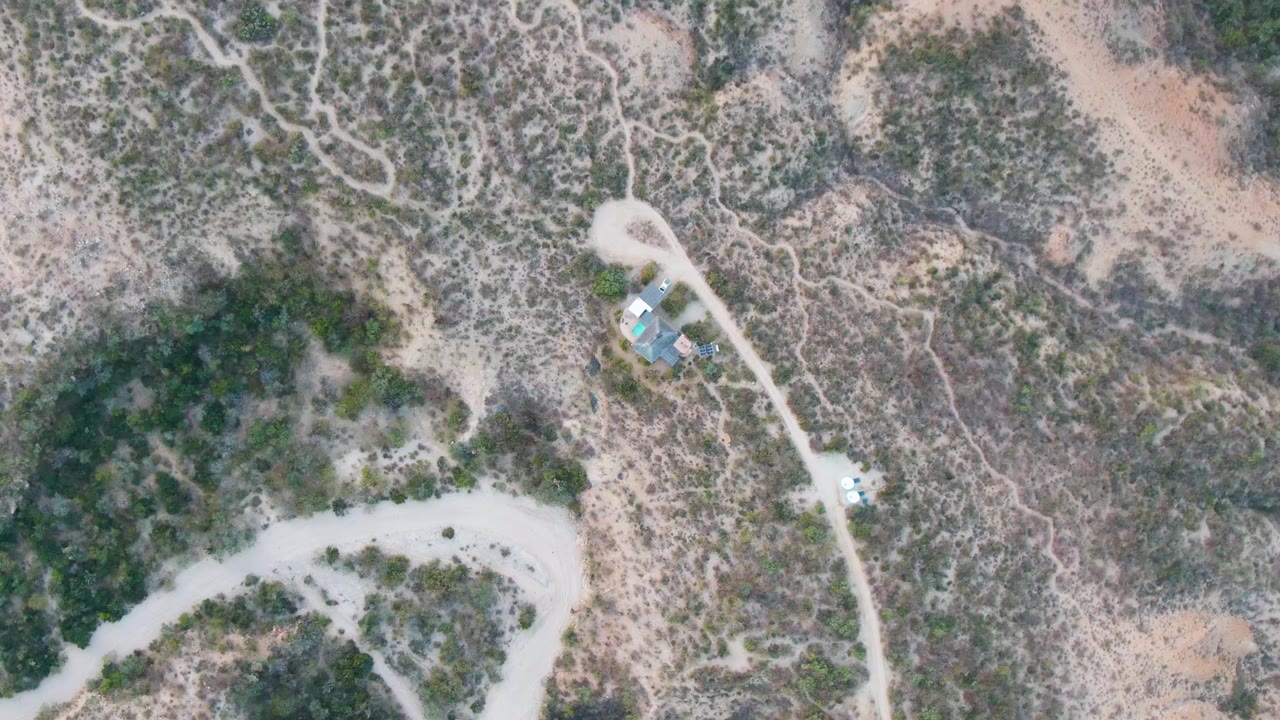 Overhead frame from Cabo Pulmo, Baja California Sur showing a winding dirt road, patchy desert vegetation, tan soil, and no visible people.