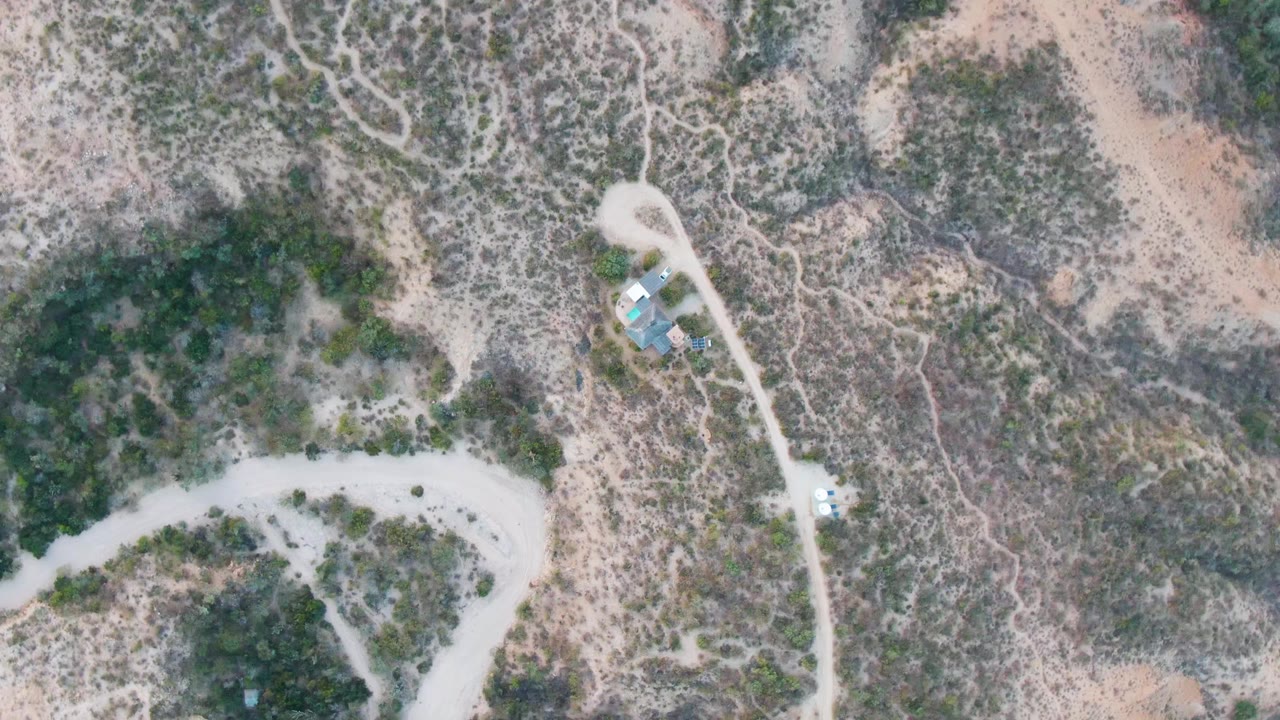 High aerial frame of desert brush, road bends, and a small vehicle.