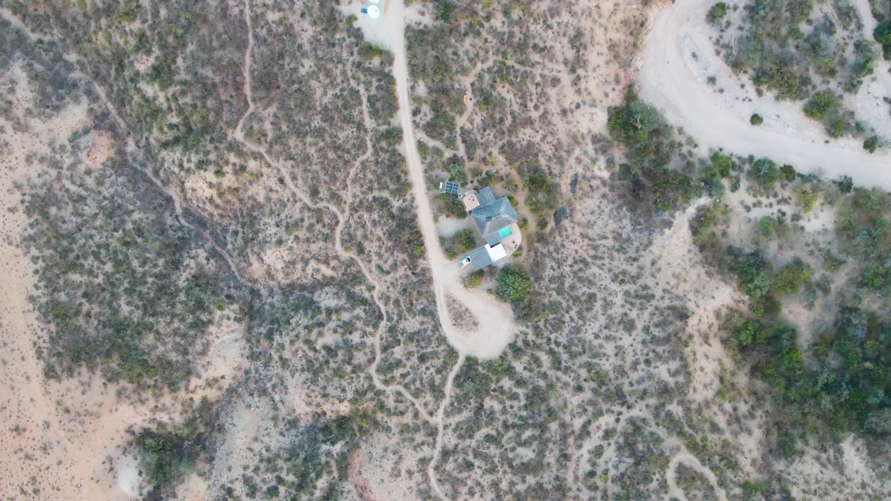 Overhead desert landscape with unpaved roads, scrub, house, and vehicle.