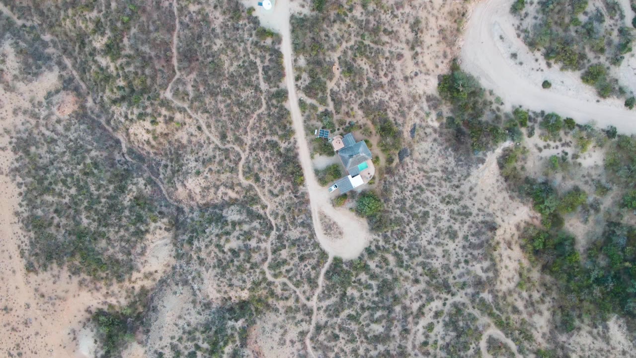 Overhead view in Cabo Pulmo, Baja California Sur showing a small house beside pale dirt roads in scrubby desert terrain, with no visible people.