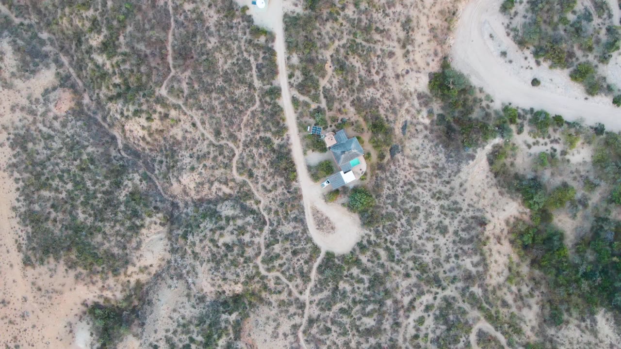 Small desert house beside a pale dirt road from above.