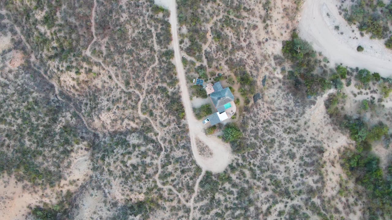 Overhead view in Cabo Pulmo, Baja California Sur, showing a pale dirt road, small isolated building, scrubby desert terrain, and no visible people at the start of the clip.