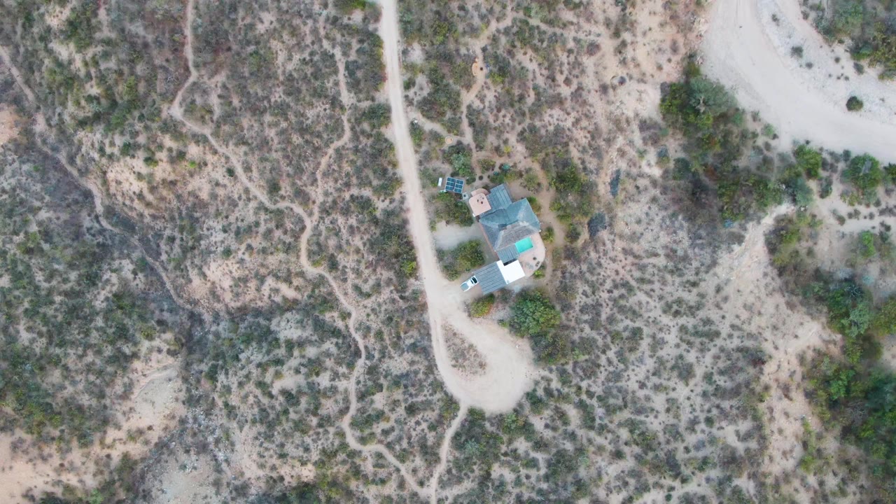 Dirt road and building cluster seen from above in arid terrain.