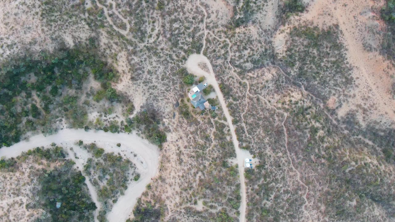 Overhead desert road scene with sparse vegetation and a small structure cluster.
