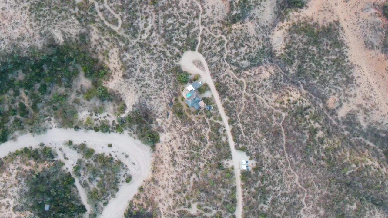 Overhead frame from Cabo Pulmo, Baja California Sur showing pale dirt roads, dry hillside scrub, a small blue and white structure near the road, and no visible people.