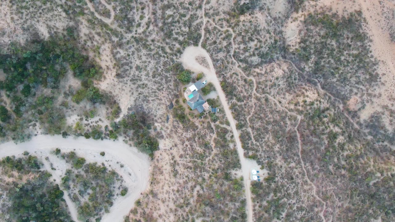 Desert road and scrubland from above with a white vehicle near small structures.