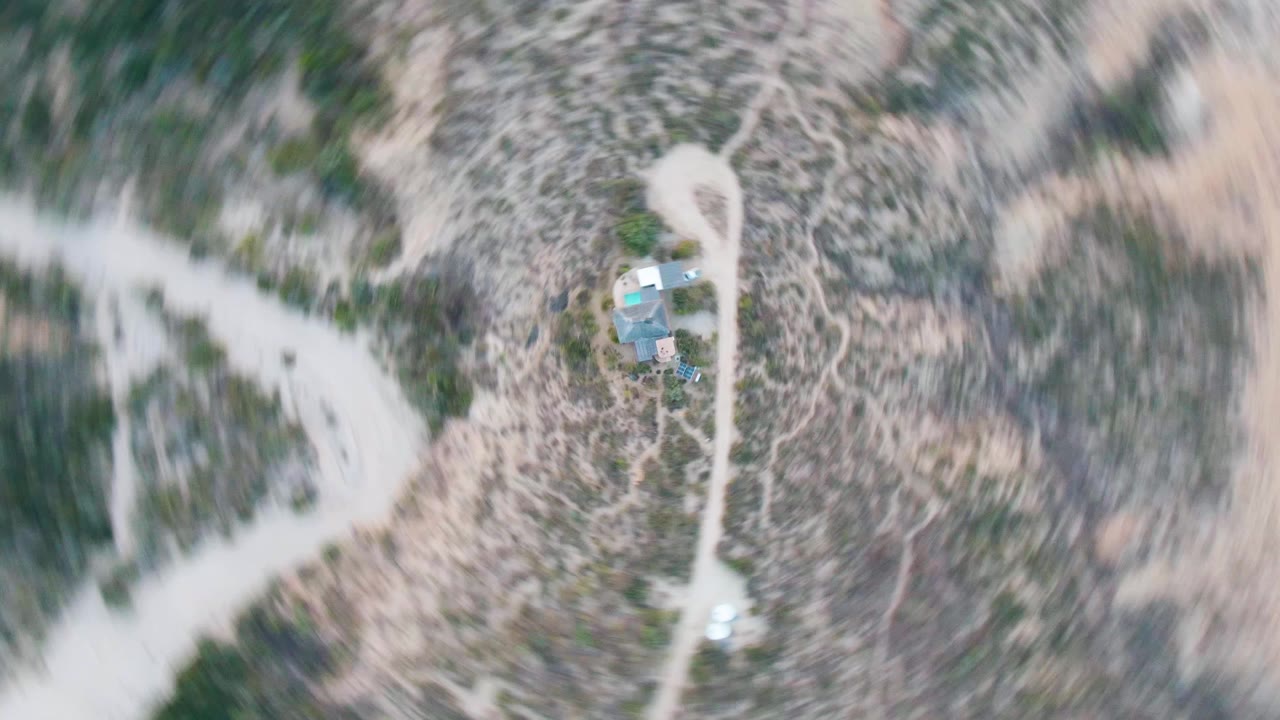 High overhead view in Cabo Pulmo, Baja California Sur, showing a small cabin compound near pale dirt roads, scrubby desert vegetation, and no visible people.
