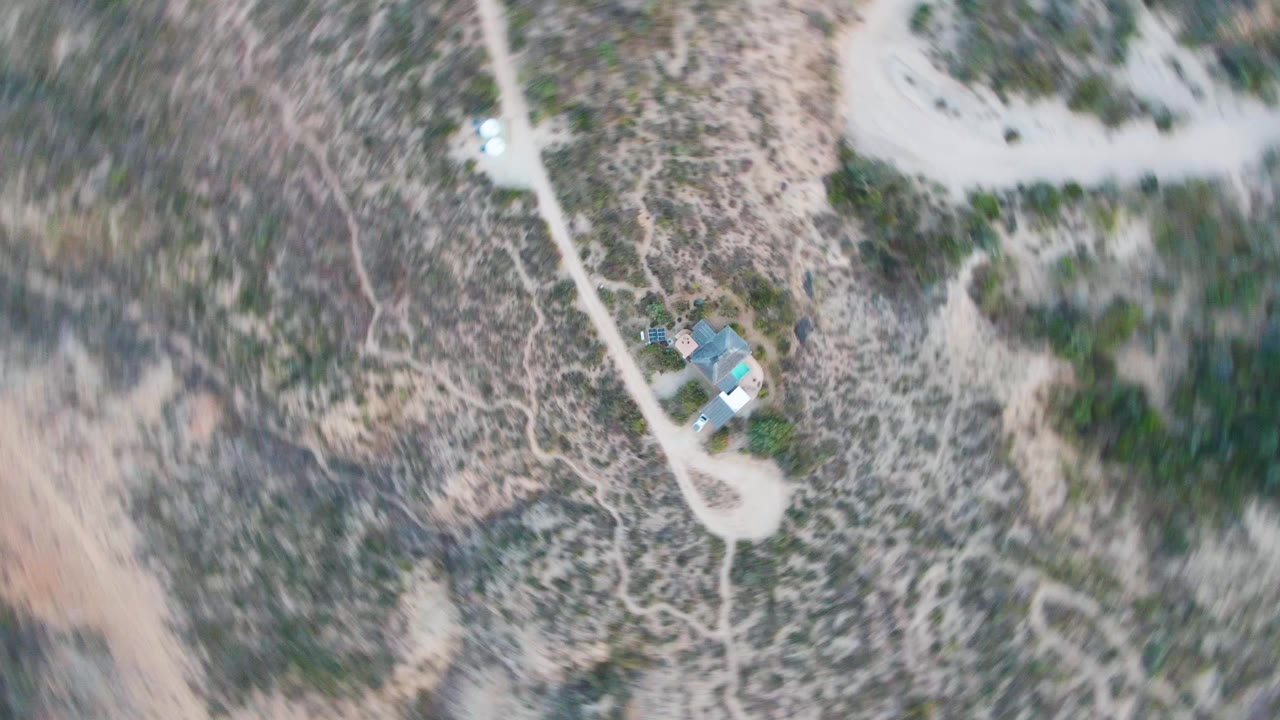 Overhead Cabo Pulmo frame showing a small light-roofed structure beside branching pale dirt roads, mottled scrubland, and no visible people.