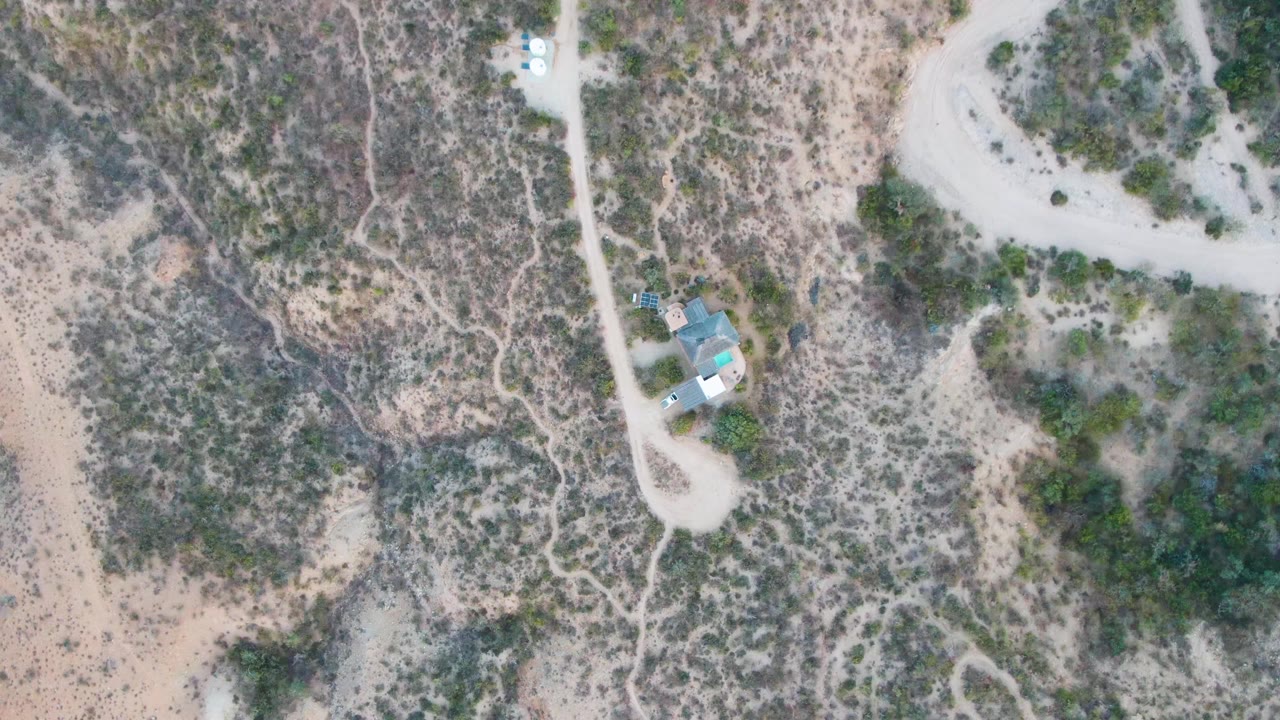 Second frame shows the Cabo Pulmo dirt road and nearby structure shifted slightly in the overhead composition, with scrub-covered terrain and no visible people.