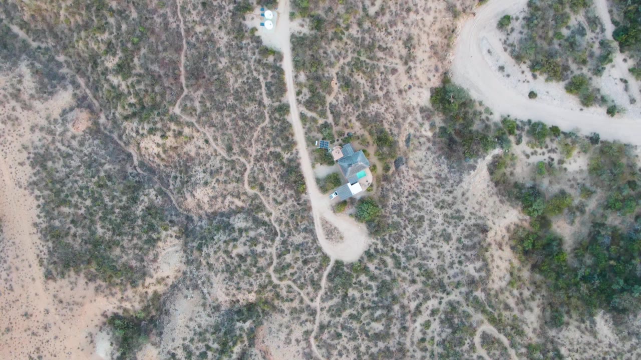 Overhead desert scene with dirt road, scrub, and a small white vehicle.