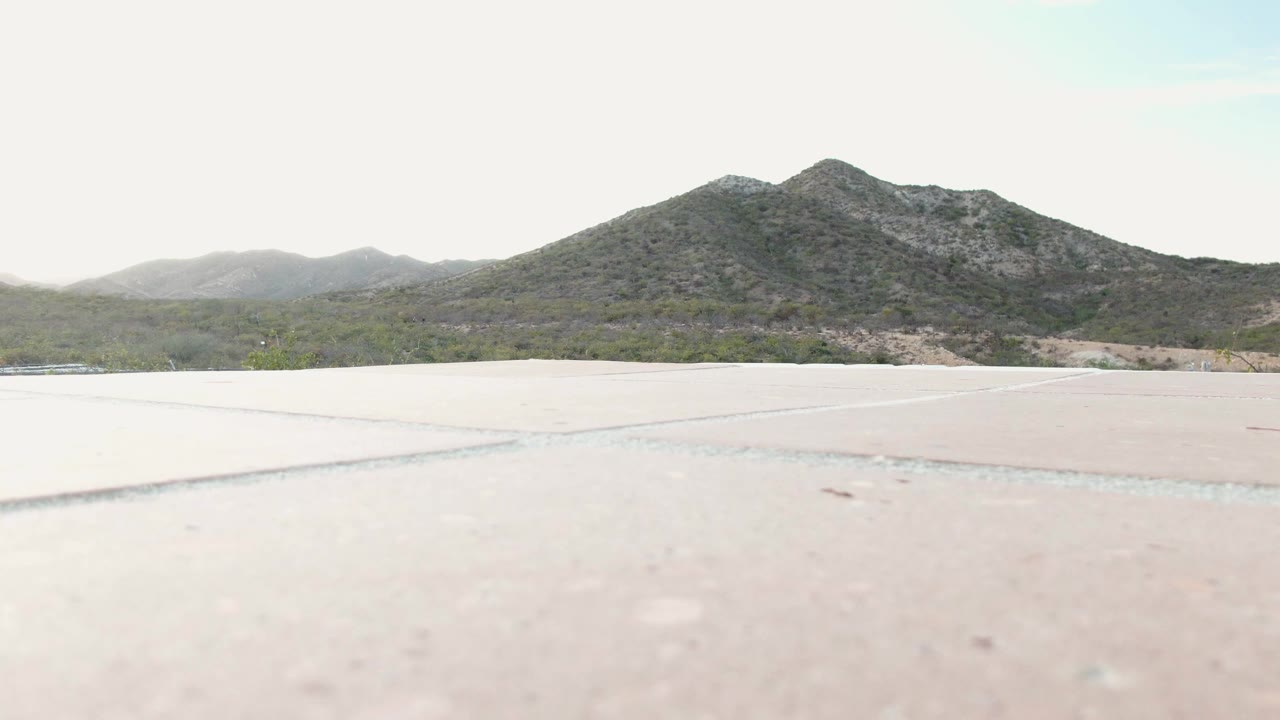 Second frame of Cabo Pulmo, Baja California Sur, showing the pale concrete plane, a thin band of dry terrain, distant green-gray mountains, and no visible people.