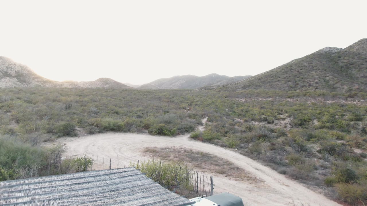 Thatched roof edge appearing below a desert road and hills