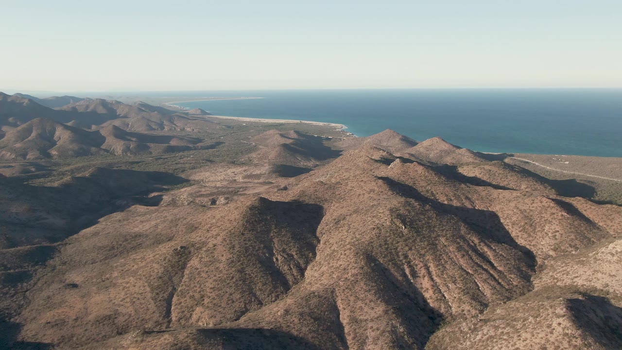 Aerial view of rocky desert mountains with ocean on the horizon.