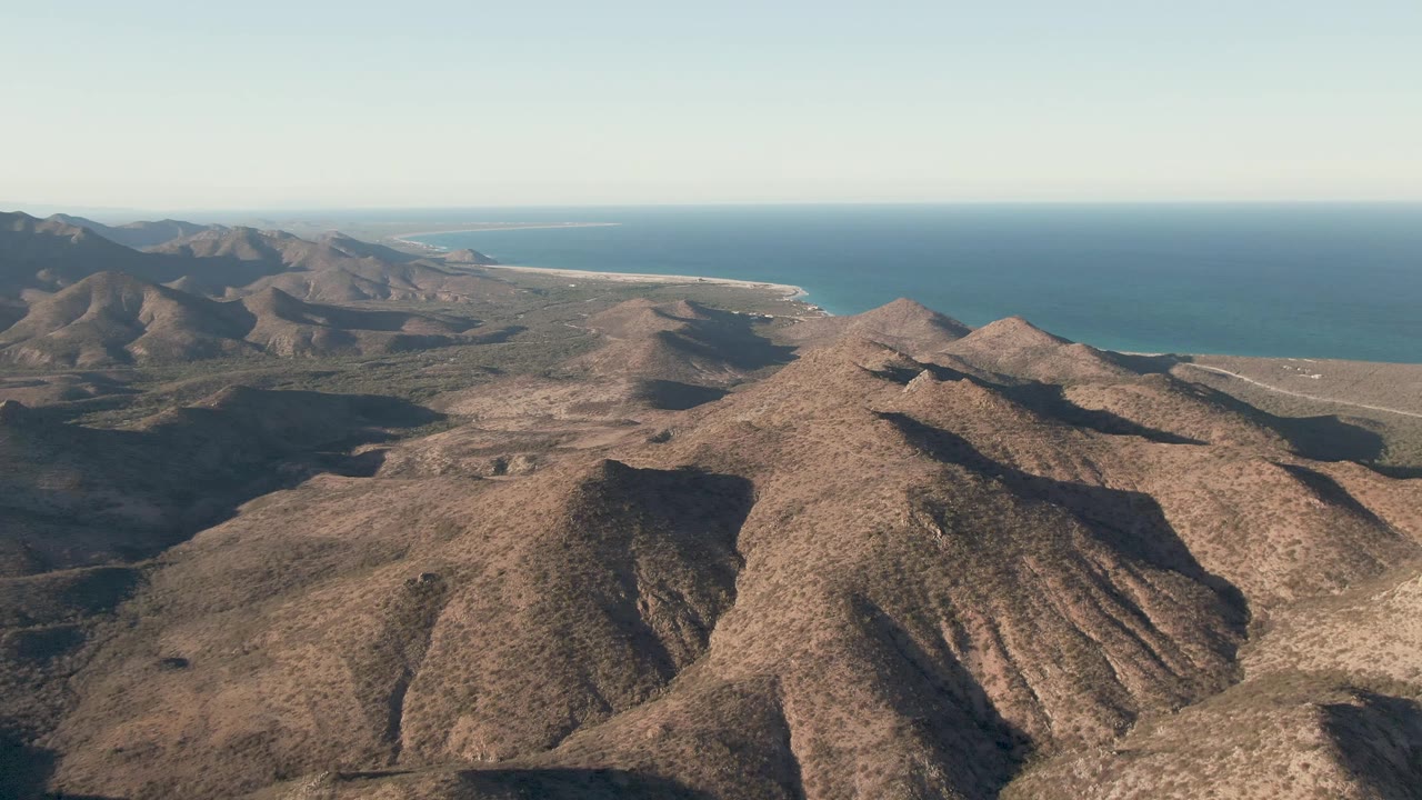 At 0:01, the Cabo Pulmo aerial view keeps the central rocky ridge in frame while darker valleys and the ocean horizon remain visible, with no visible people.