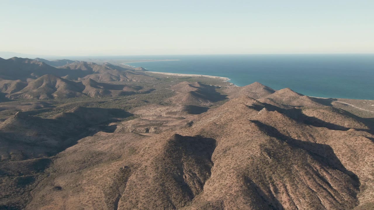 Aerial view of dry mountain ridges with ocean in the distance.