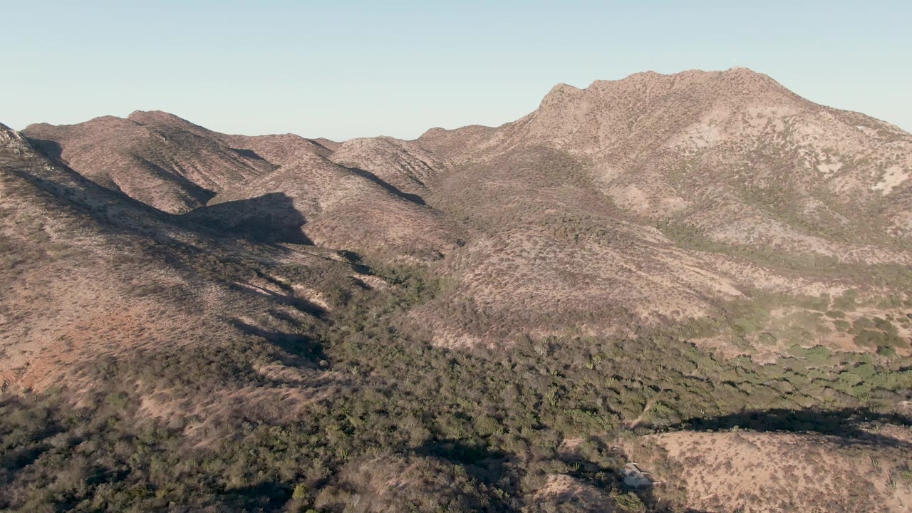 Aerial view in Cabo Pulmo showing the central mountain ridge, darker shadow across the left slope, scattered scrub, and no visible people.