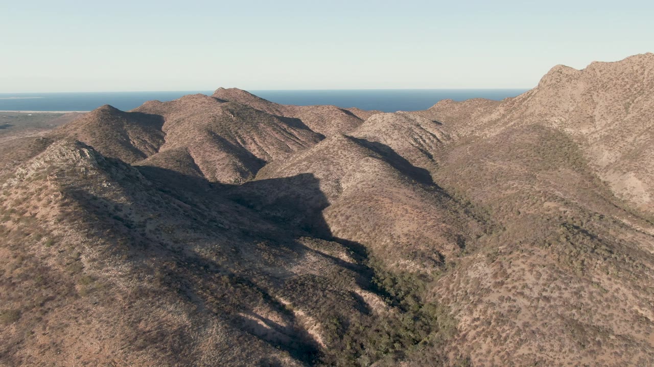 Wide aerial of dry ridges with blue sea behind them