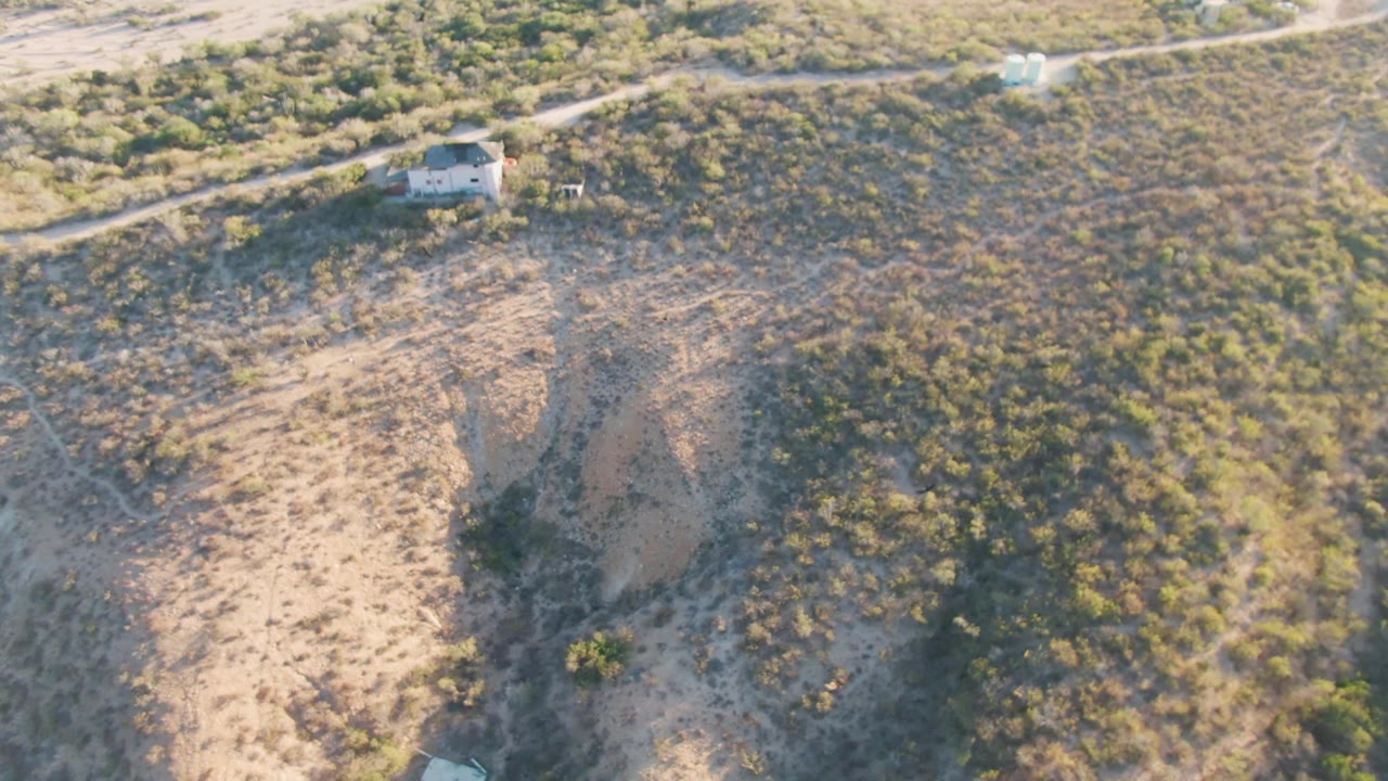 Aerial desert hillside with winding dirt track and brush.