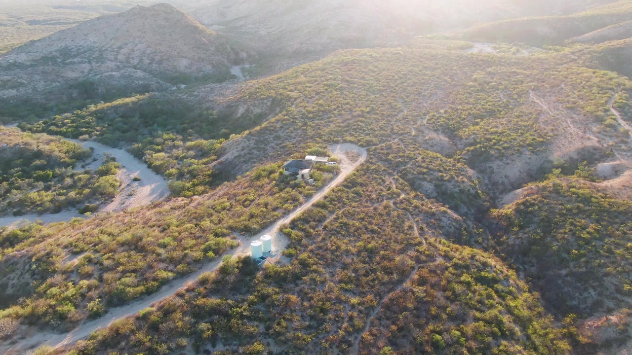 Aerial view of a pale road curving past hills and sparse green vegetation.