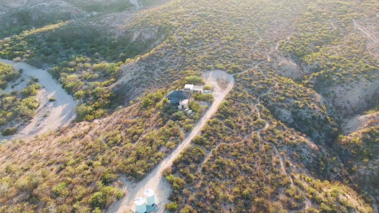 Drone view of a dirt road curving past a small hillside structure.
