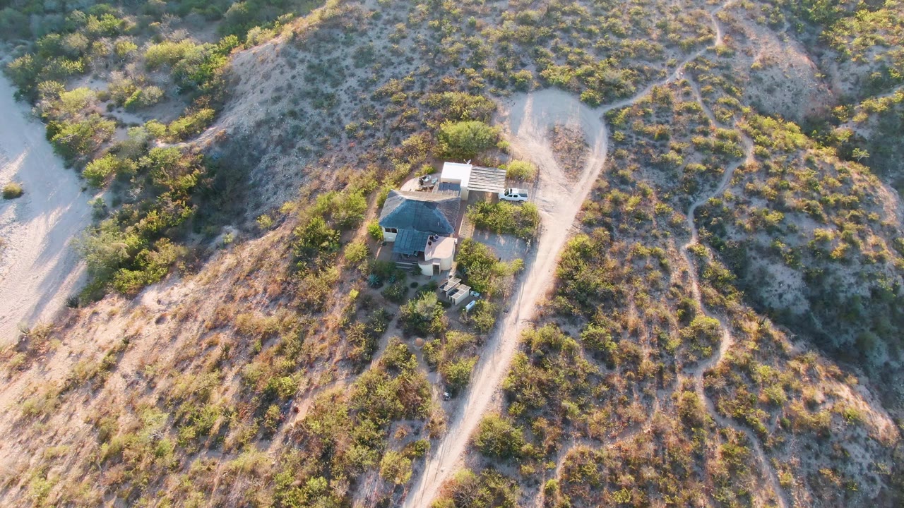 Aerial frame from Cabo Pulmo, Baja California Sur showing a small hilltop house beside pale dirt roads, scattered green scrub, and no visible people at the start of the clip.