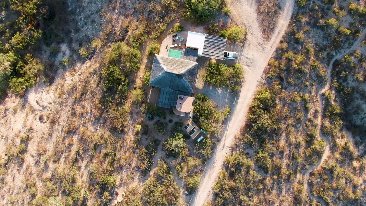 Drone view of a house, driveway, and dirt road through arid terrain.