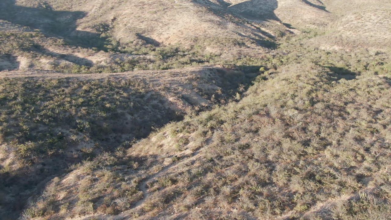 Closer aerial angle over a scrub-covered desert hillside.