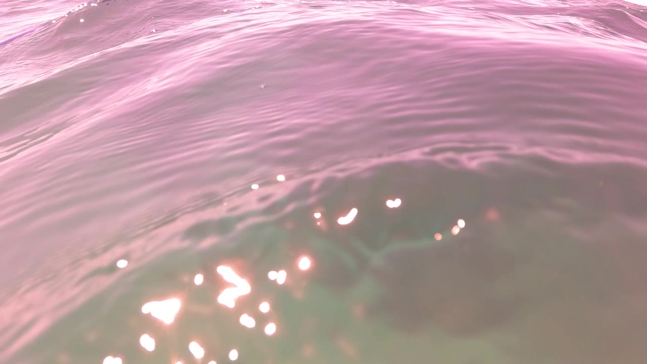 Pink-hued ocean surface in San Jose Del Cabo with close ripples, bright reflected highlights, and no visible people.