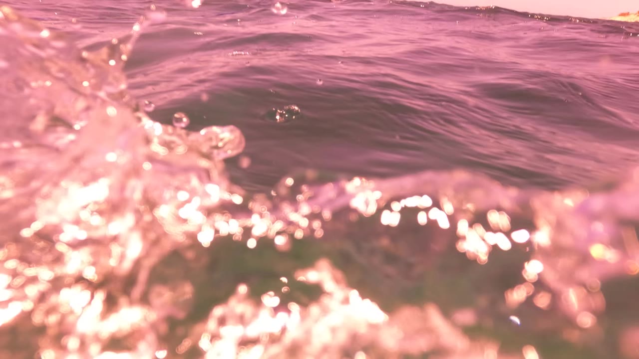 Pink ocean water in San Jose Del Cabo splashes near the lens, with bright highlights and no visible people.