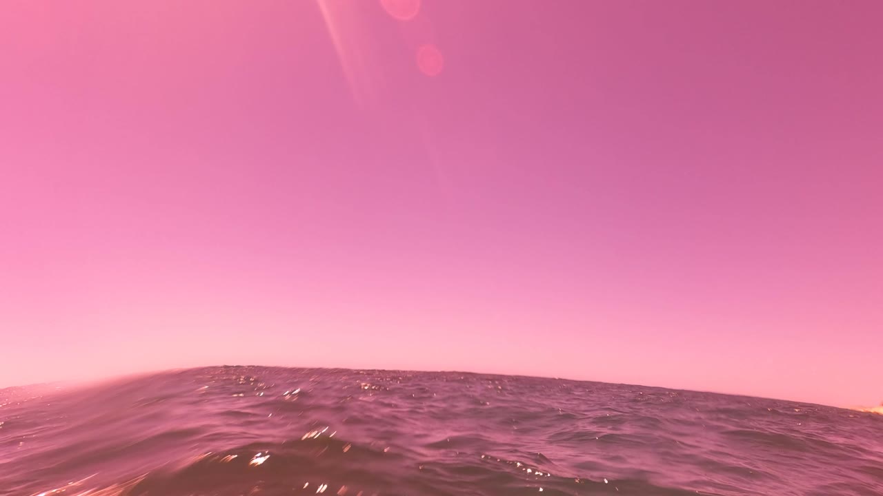 Pink-lit ocean surface near San Jose del Cabo with a low dark wave line across the lower frame and no visible people.