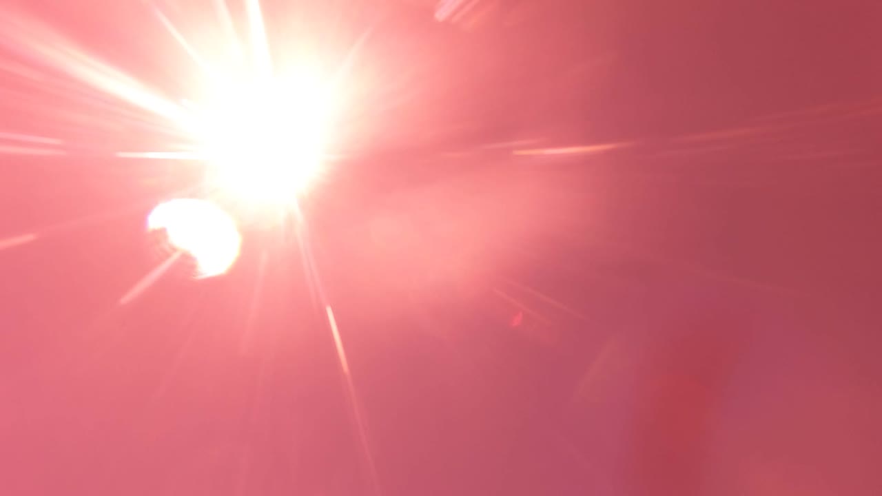 At 0:00, a bright sun flare fills the upper left of a pink-red San Jose del Cabo sky while a small white moon shape sits nearby, with no visible people.