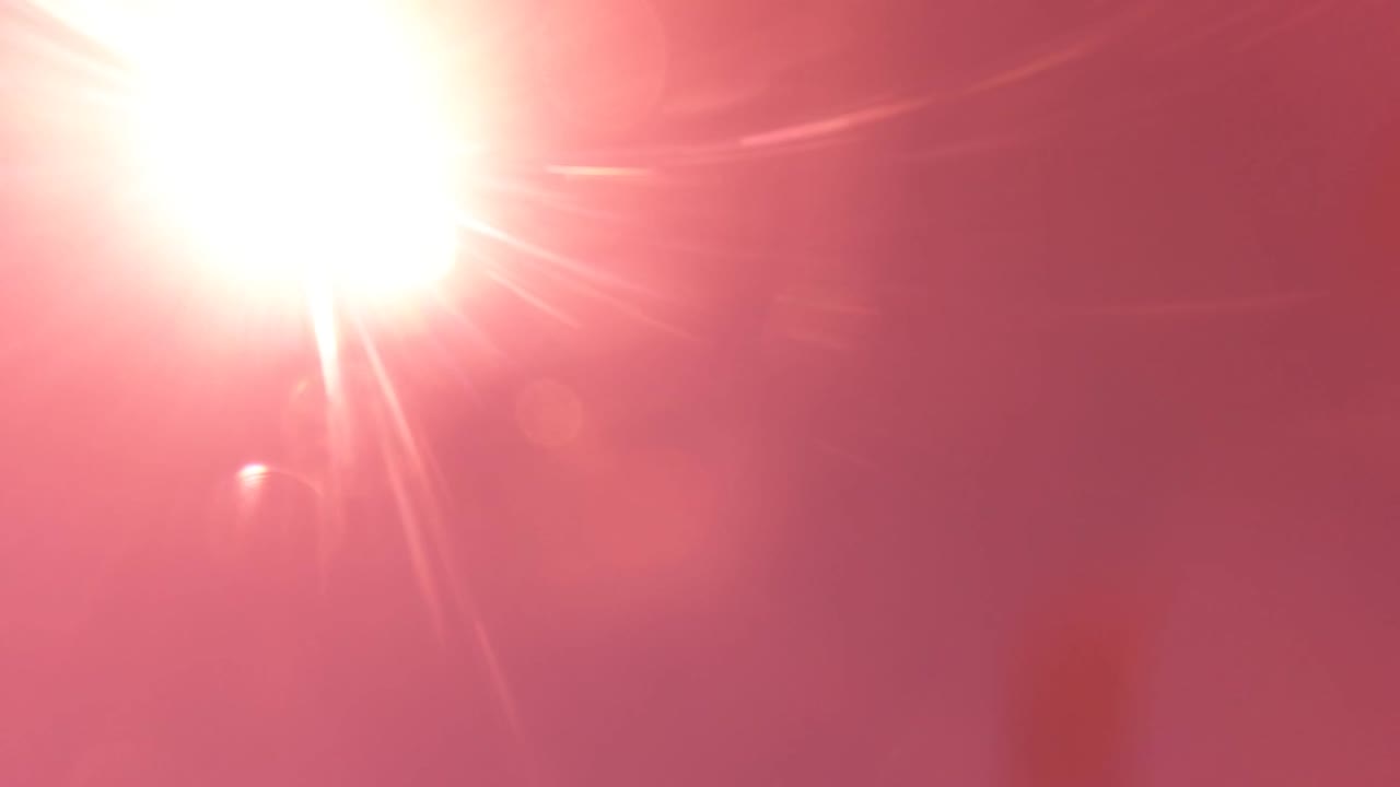 At 0:02, the sun glare expands near the top of the San Jose del Cabo frame, with faint circular lens flares across the pink-red sky and no visible people.