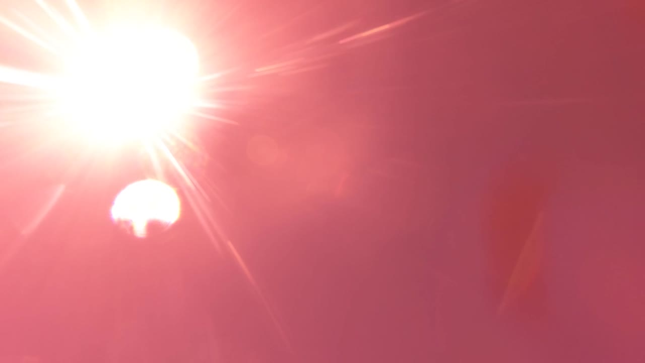 Bright sun flare and white moon shape against a saturated pink sky.