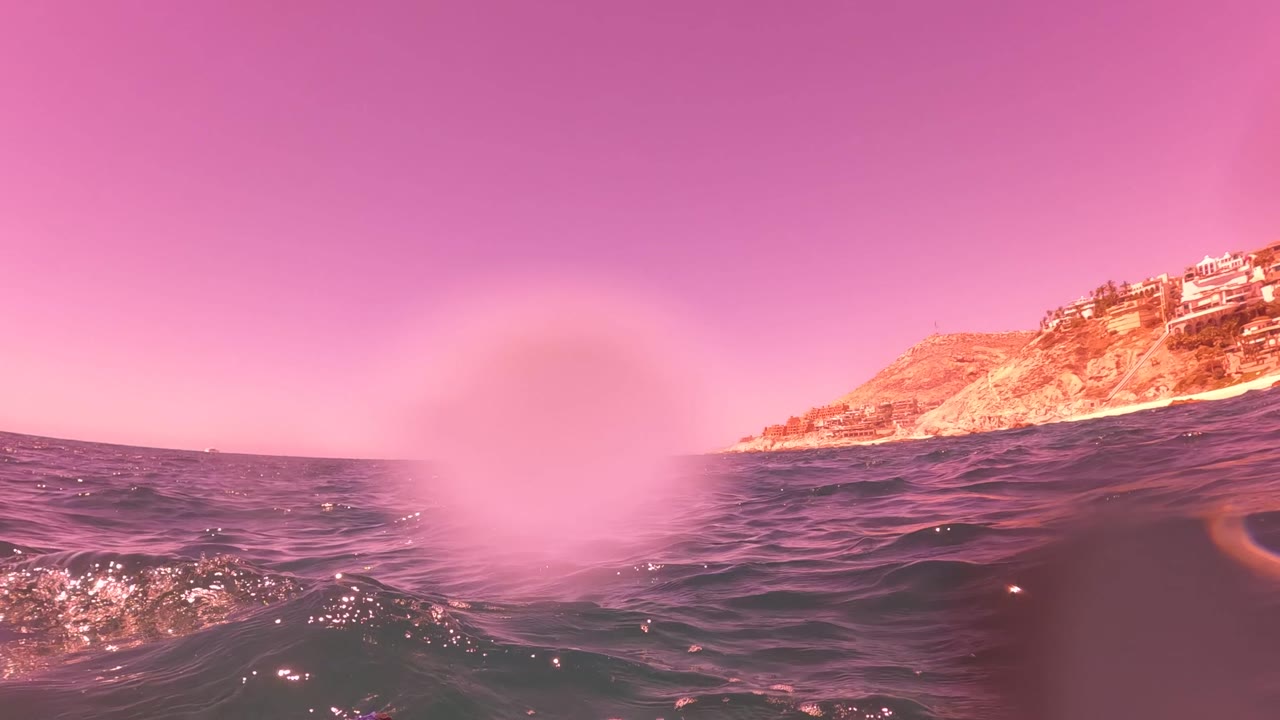 Ocean surface with distant rocky shoreline under pink tint