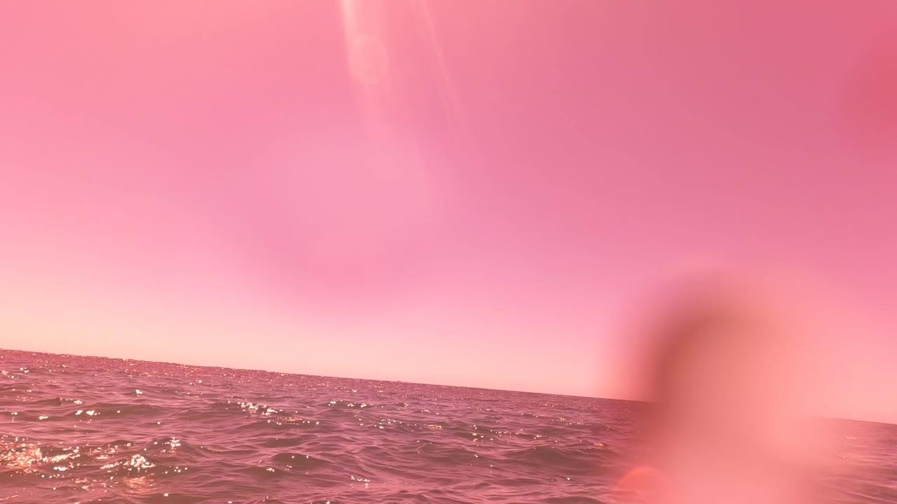 Pink-tinted San Jose del Cabo ocean horizon with rippled water, soft foreground obstruction, lens droplets, and no visible people.