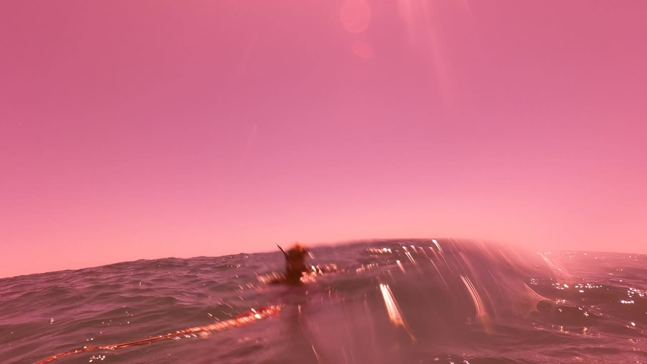 Waterline view in San Jose del Cabo with a pink sky, dark ocean waves, bright lens streaks, and blurred water droplets across the frame.
