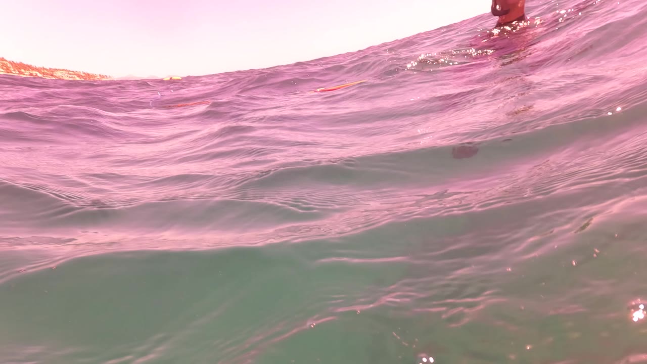 A low waterline frame in San Jose Del Cabo shows dark rolling ocean surface, distant beach and rocky shoreline, pink sky, and no clearly visible people.