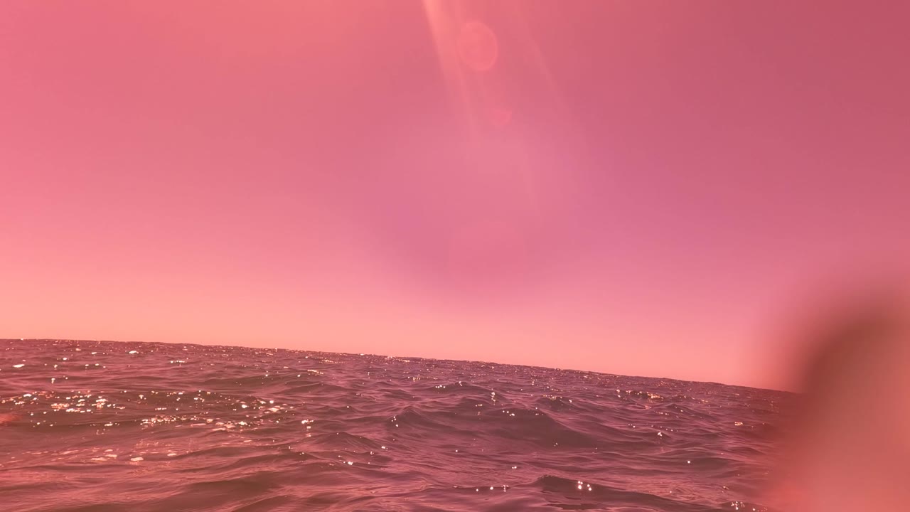 Pink-hued ocean surface near San Jose del Cabo with a low horizon, soft water blur in the foreground, and no visible people.