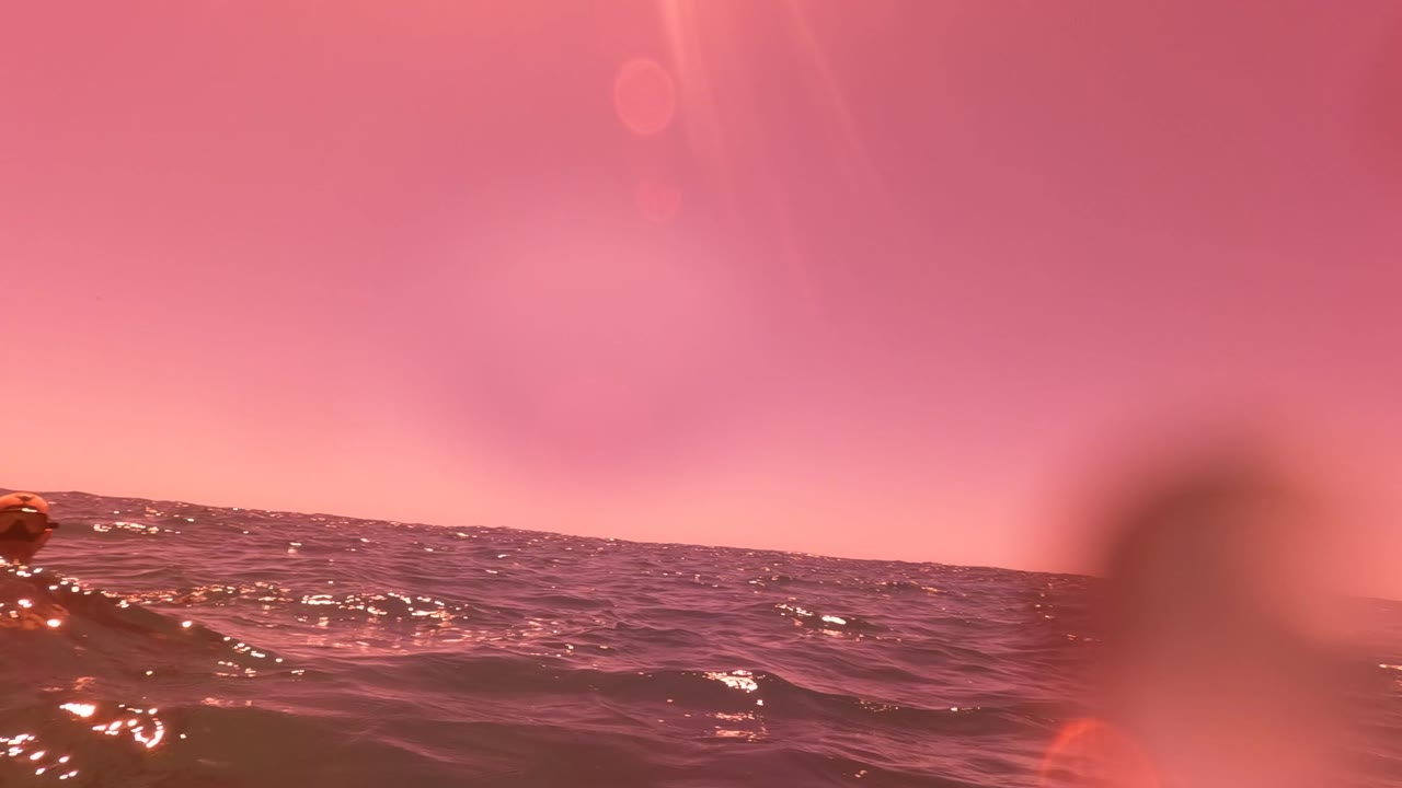 Pink and purple ocean water near San Jose del Cabo with sun glints on small waves and blurred foreground water shapes, with no visible people.